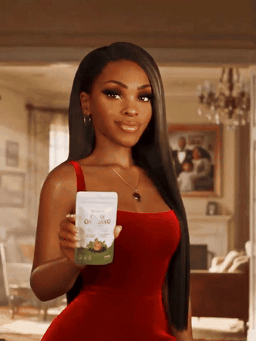 A woman in a red dress smiling and holding up her Resilia Oil of Oregano pouch