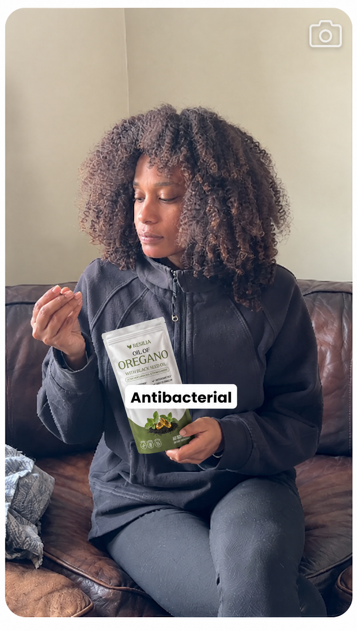 A real customer on her couch holding her Resilia softgel and pouch